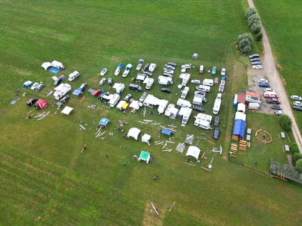 Luftaufnahme eines Modellflugplatzes mit zahlreichen wei&szlig;en Wohnwagen, bunten Zelten und Modellflugzeugen auf gr&uuml;ner Wiese