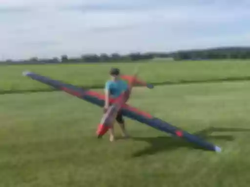 Rot-schwarzes Segelflugmodell auf grüner Rasenfläche, daneben stehend eine Person mit Sonnenbrille und Baseballcap