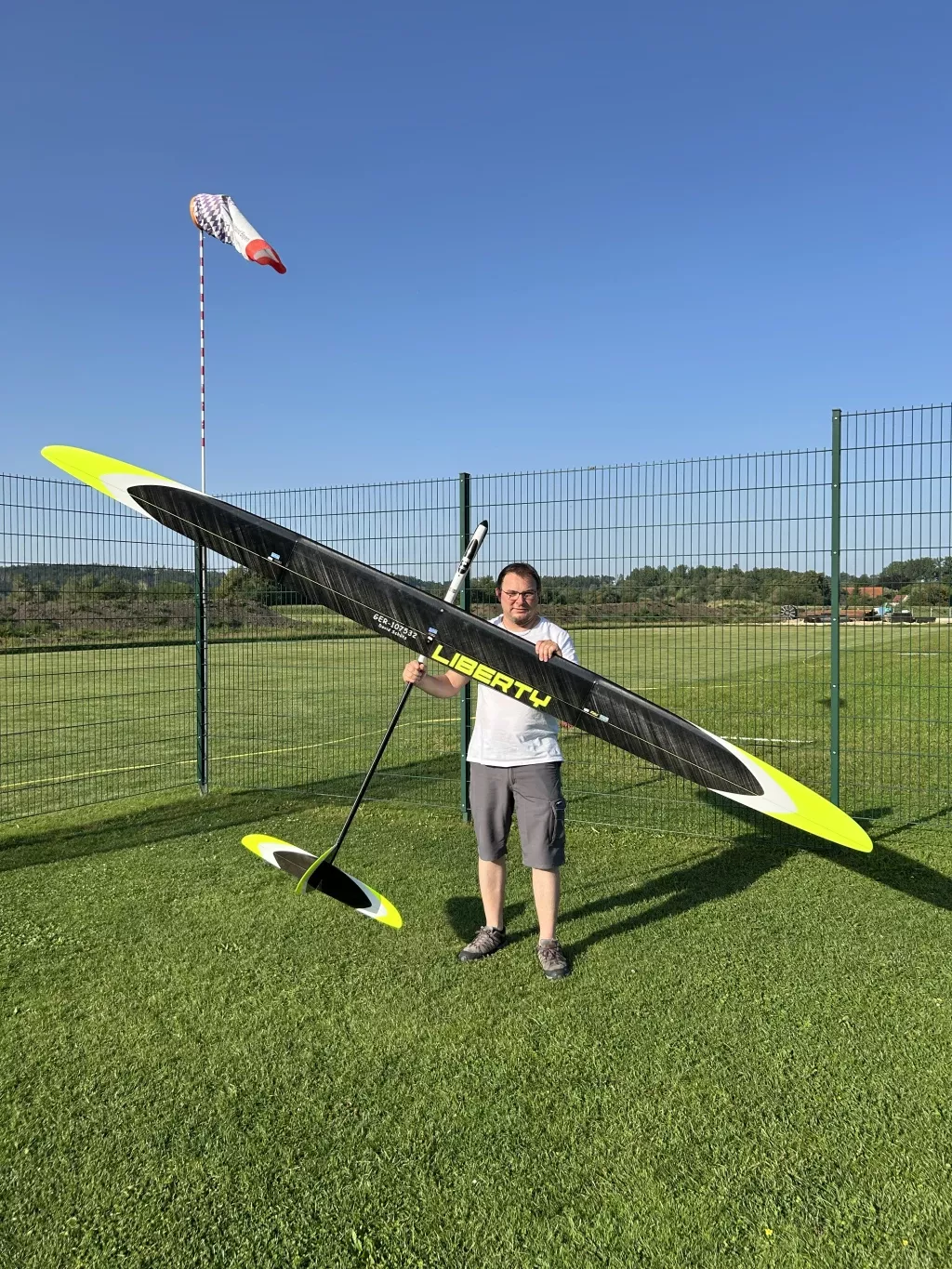 Gro&szlig;es schwarzes und gelbes Segelflugmodell mit Schriftzug 'Liberty' auf gr&uuml;nem Rasenplatz, daneben Windsack und Person