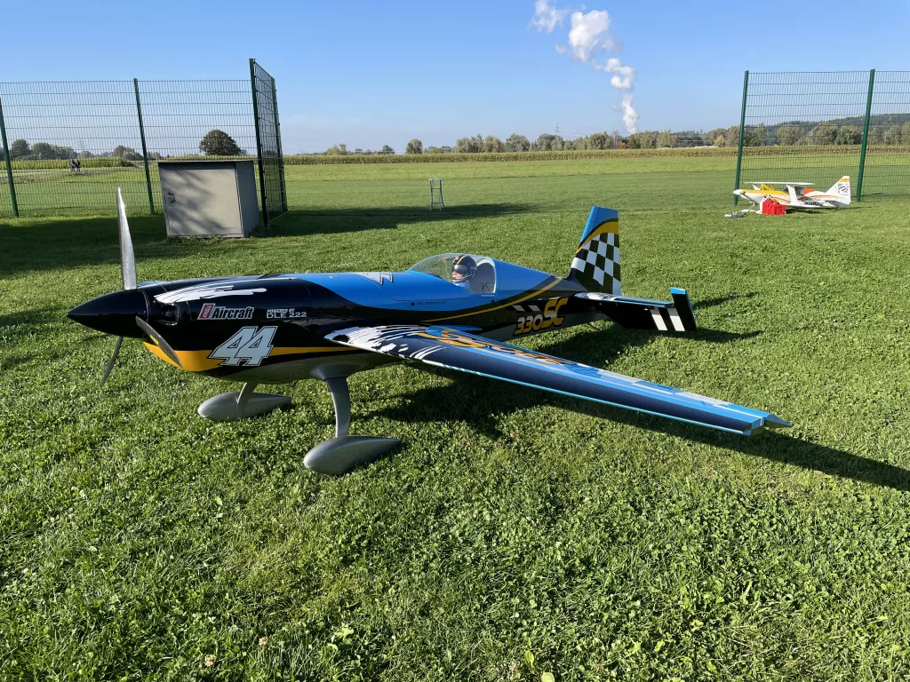 Blau-schwarzes Kunstflug-Modellflugzeug mit Nummer 44 auf gr&uuml;ner Rasenfl&auml;che, Zaun und Wiese im Hintergrund