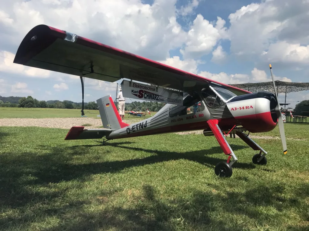 Rotwei&szlig;-silbernes Modellflugzeug AJ-14RA auf gr&uuml;ner Wiese mit Wolkenhimmel, Kennzeichen D-ERNJ