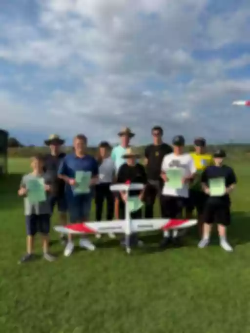 Gruppenphoto von 11 Personen unterschiedlichen Alters mit Modellflugzeug und grünen Urkunden auf Rasenplatz