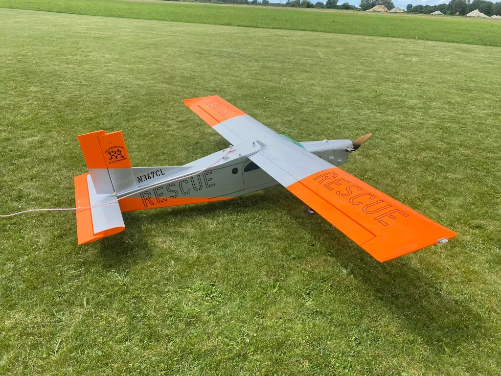 Wei&szlig;es und orangefarbenes Modellflugzeug mit 'Rescue'-Beschriftung auf gr&uuml;ner Rasenfl&auml;che, Kennzeichen N347CL