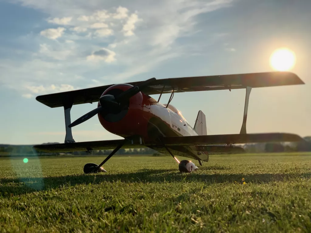 Roter Vintage-Doppeldecker auf gr&uuml;ner Wiese, Morgensonne im Hintergrund, Flugzeug steht auf Graslandebahn